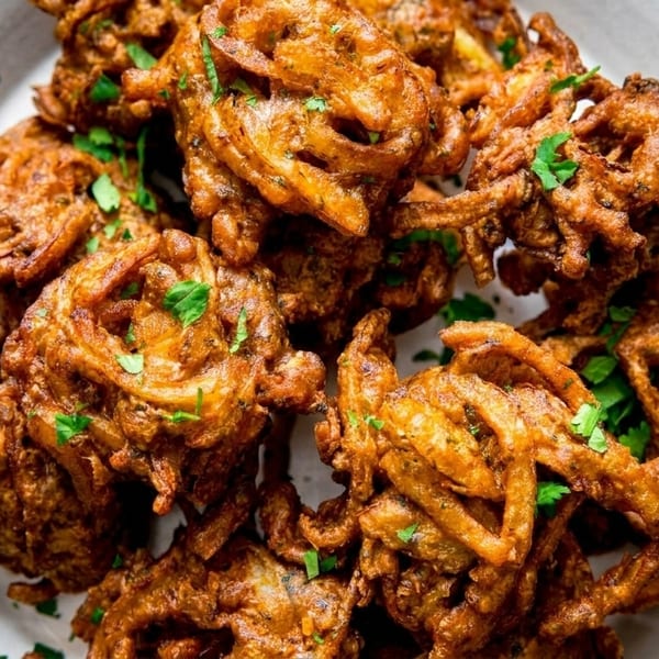 Crispy golden-brown onion bhaji fritters, garnished with fresh green cilantro, on a white plate.