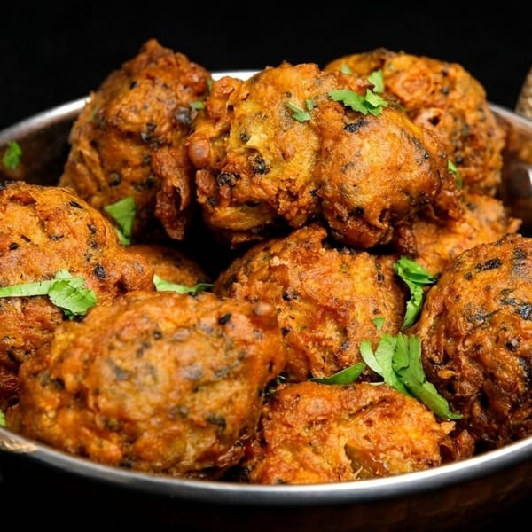 Golden-brown pakoras, garnished with fresh cilantro, served in a traditional copper bowl.