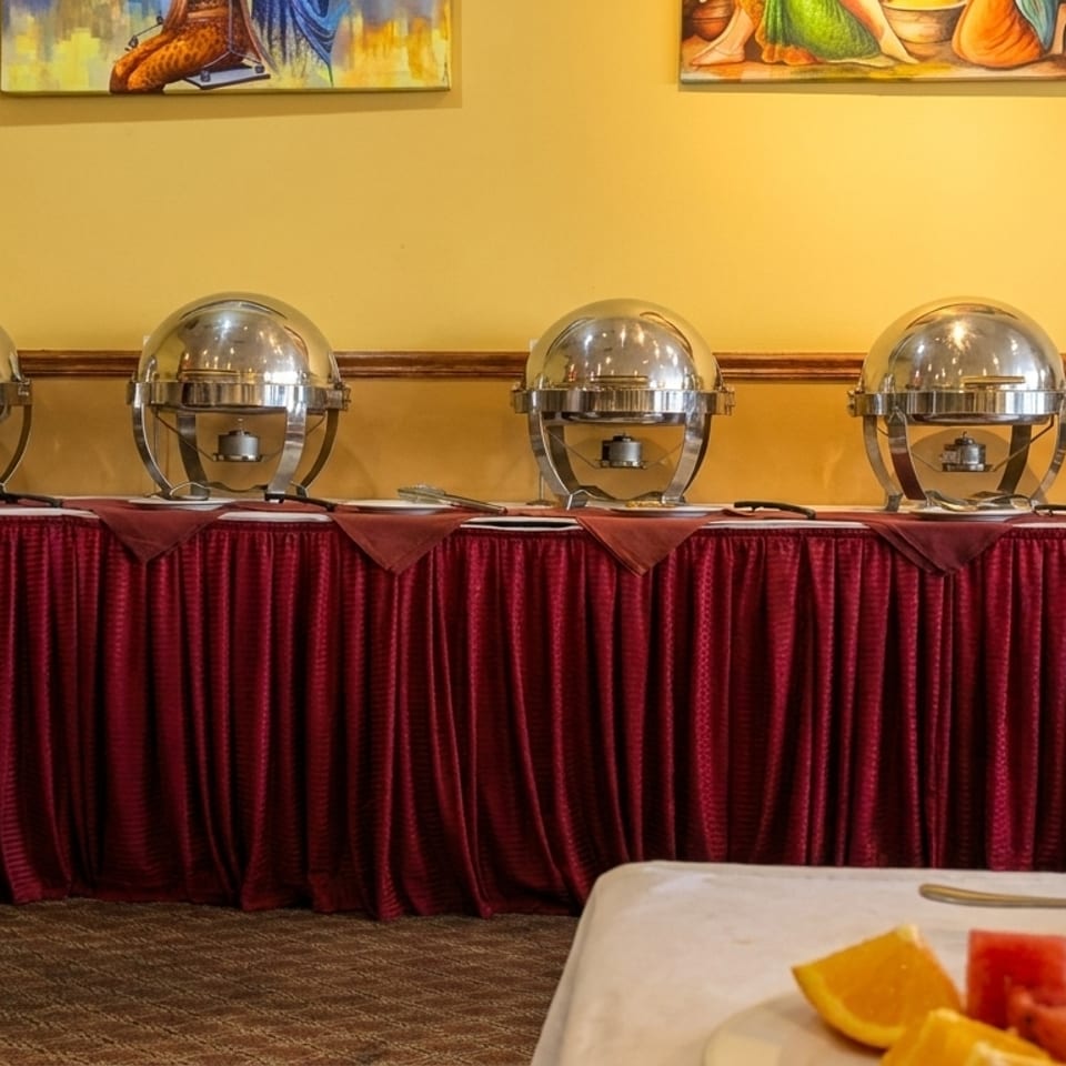 A buffet line with four silver chafing dishes on a red-skirted table, with fruit in the foreground.