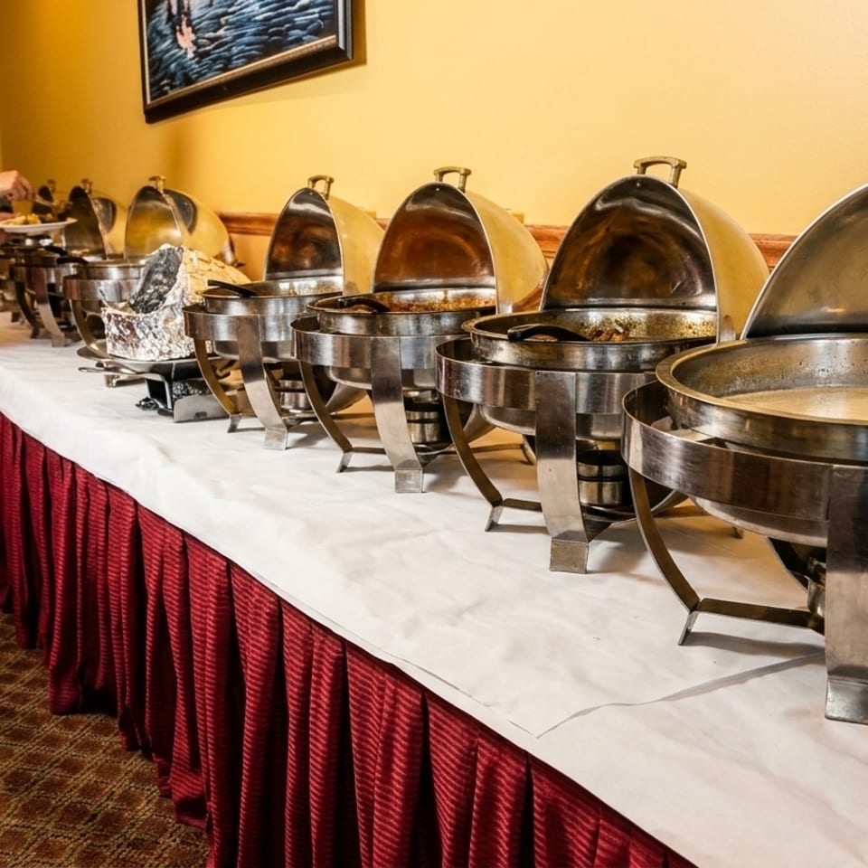 A man serving himself from a buffet line with multiple chafing dishes filled with food.