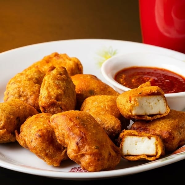 Golden-fried paneer pakora with a side of red dipping sauce and a red mug.